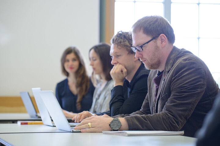 Vier Personen sitzen nebeneinander an Tischen und arbeiten an Laptops.
