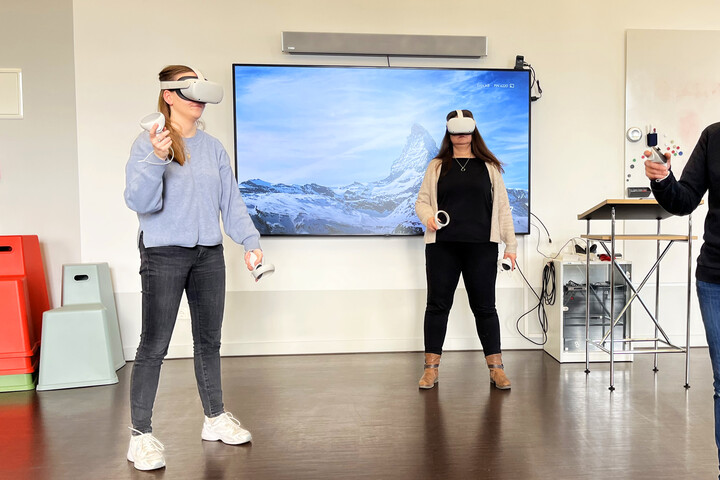 Drei Personen benutzen VR-Brillen im ExpLAB im Bibliotheksbereich Schloss Schneckenhof. An der Wand hängt ein großer Präsentationsmonitor, auf dem eine Schneelandschaft zu erkennen ist.