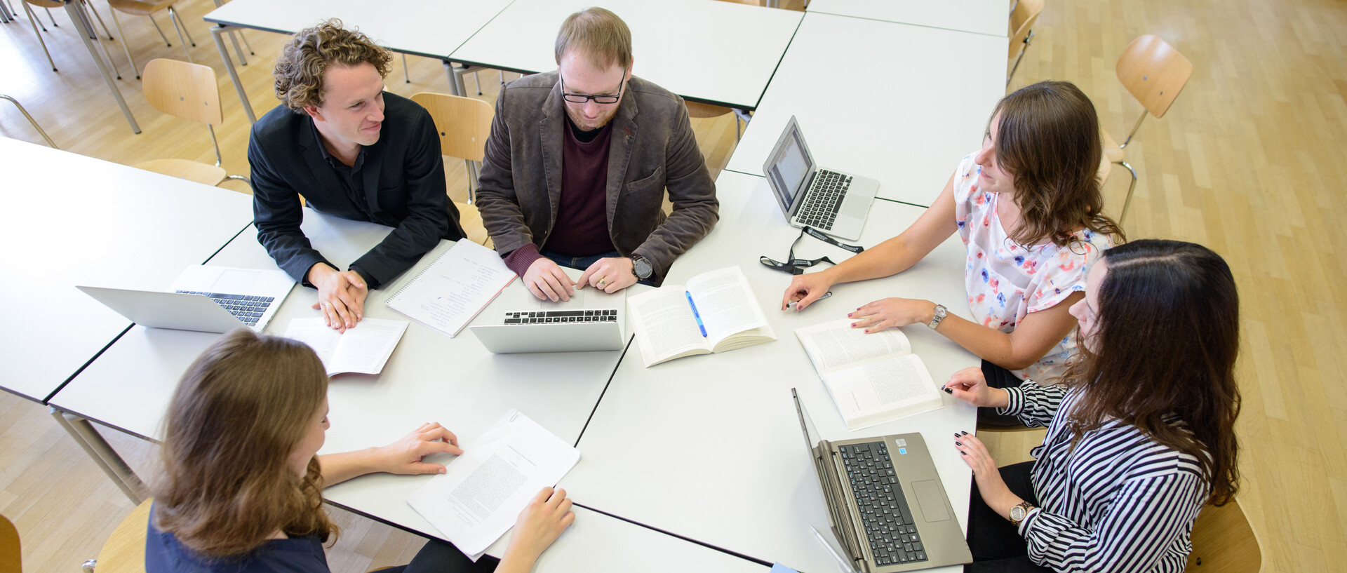Fünf Personen arbeiten gemeinsam in einem Seminarraum. Im Raum stehen Schreibtische und Laptops.