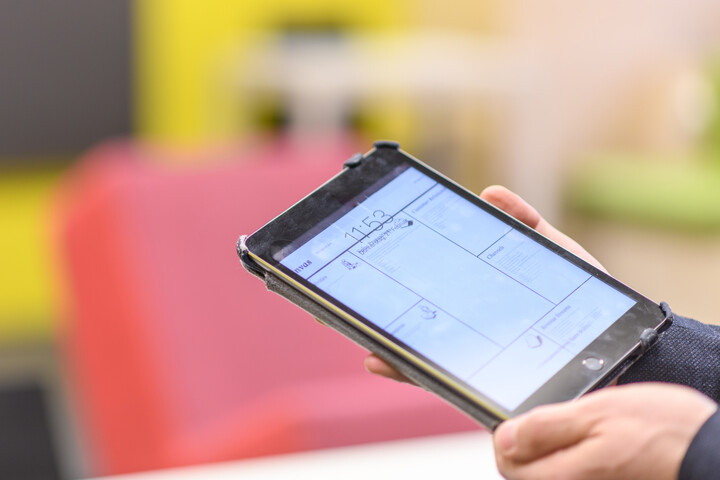 Ein E-Book-Reader wird in zwei Händen gehalten. Im Hintergrund ist die Lounge im Learning Center im Bibliotheksbereich Schloss Schneckenhof.