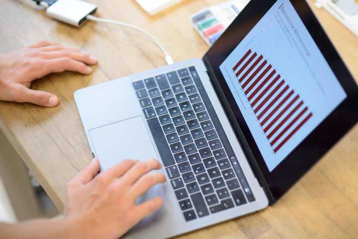 Hande schreiben an einem Laptop. Auf dem Monitor ist ein Diagramm.