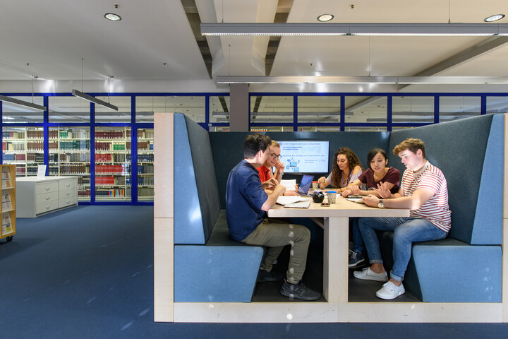 Eine Gruppe Studierender sitzt in einem blauen Kubus im Bibliotheksbereich A5. Sie sind miteinander im Gespräch.